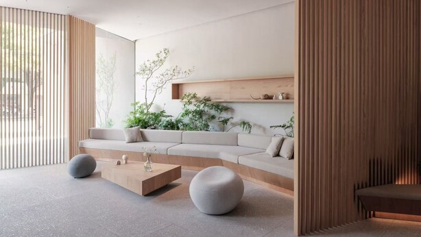 A modern living room with a sofa, two round ottomans, a wooden coffee table, and a wooden shelf with plants.