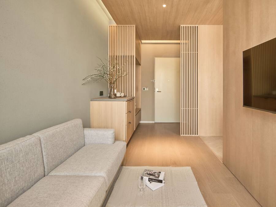 A modern living room with a sofa, a coffee table with a magazine and a glass, and a TV on the wall.