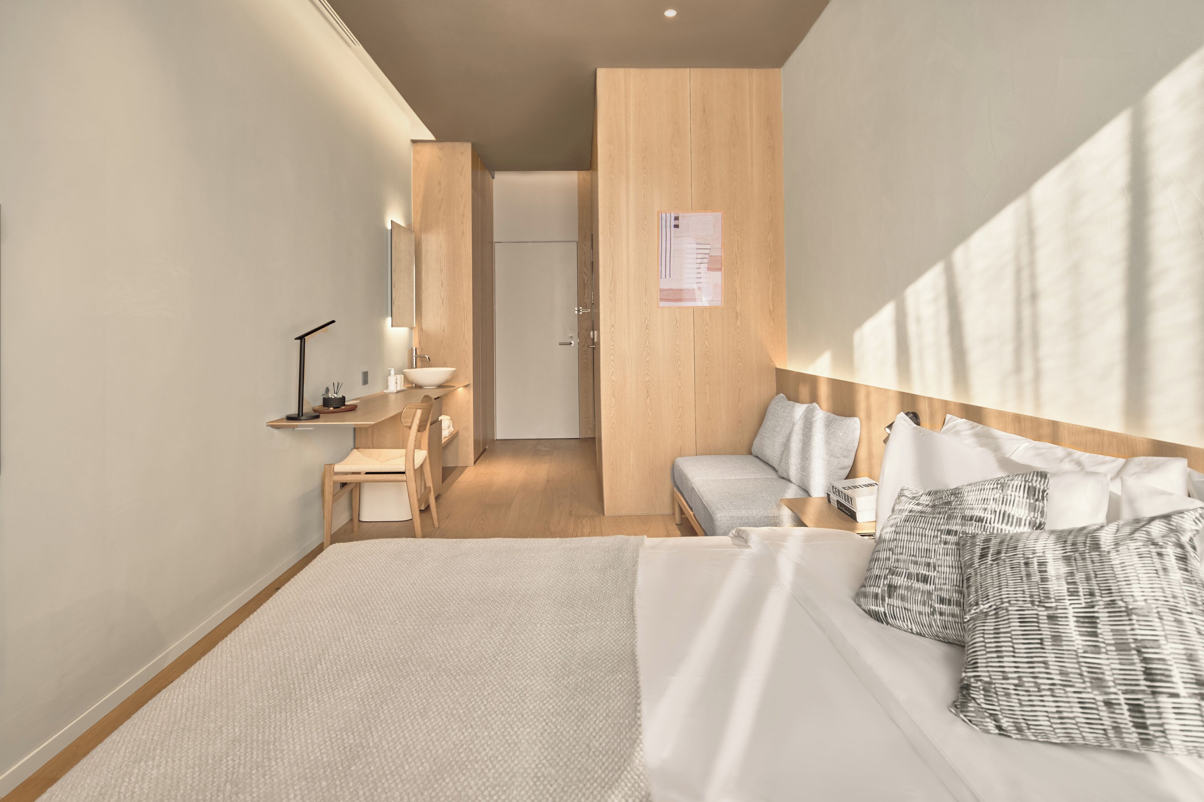 Ein modernes Hotelzimmer mit einem großen Bett, einem Schreibtisch mit Stuhl, einer kleinen Sitzecke und einem Holzschrank.