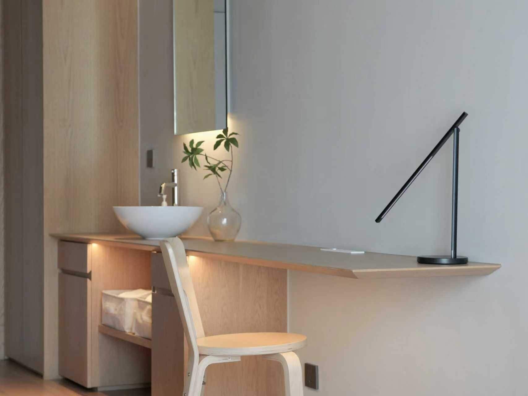Un baño moderno con tocador de madera, un lavamanos blanco, un espejo, un jarrón con una planta y una lámpara de pie.