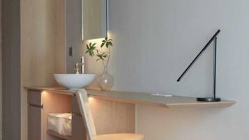 A modern bathroom with a wooden vanity, a white sink, a mirror, a vase with a plant, and a floor lamp.