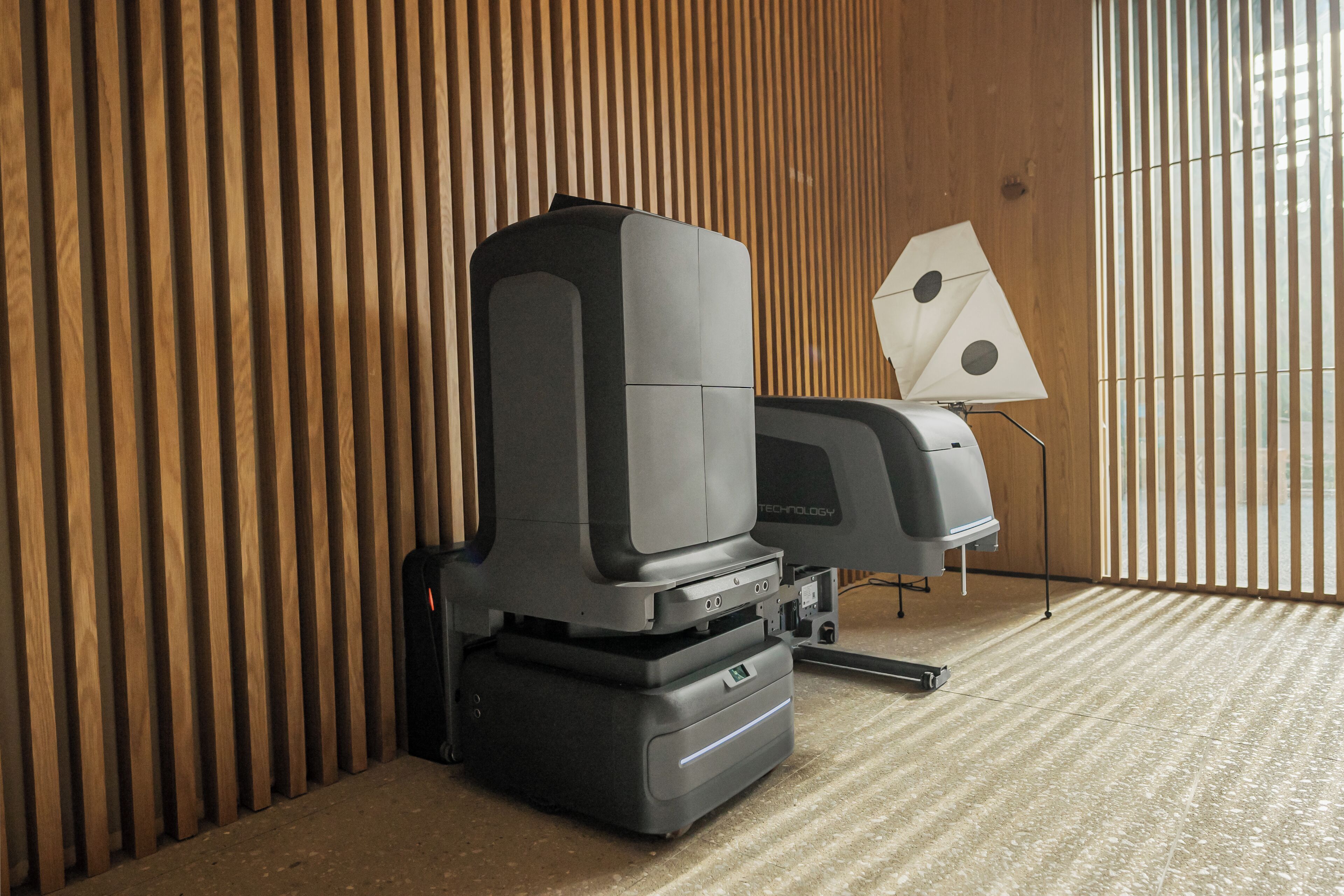A room with a large printer and a lamp on a wooden floor.