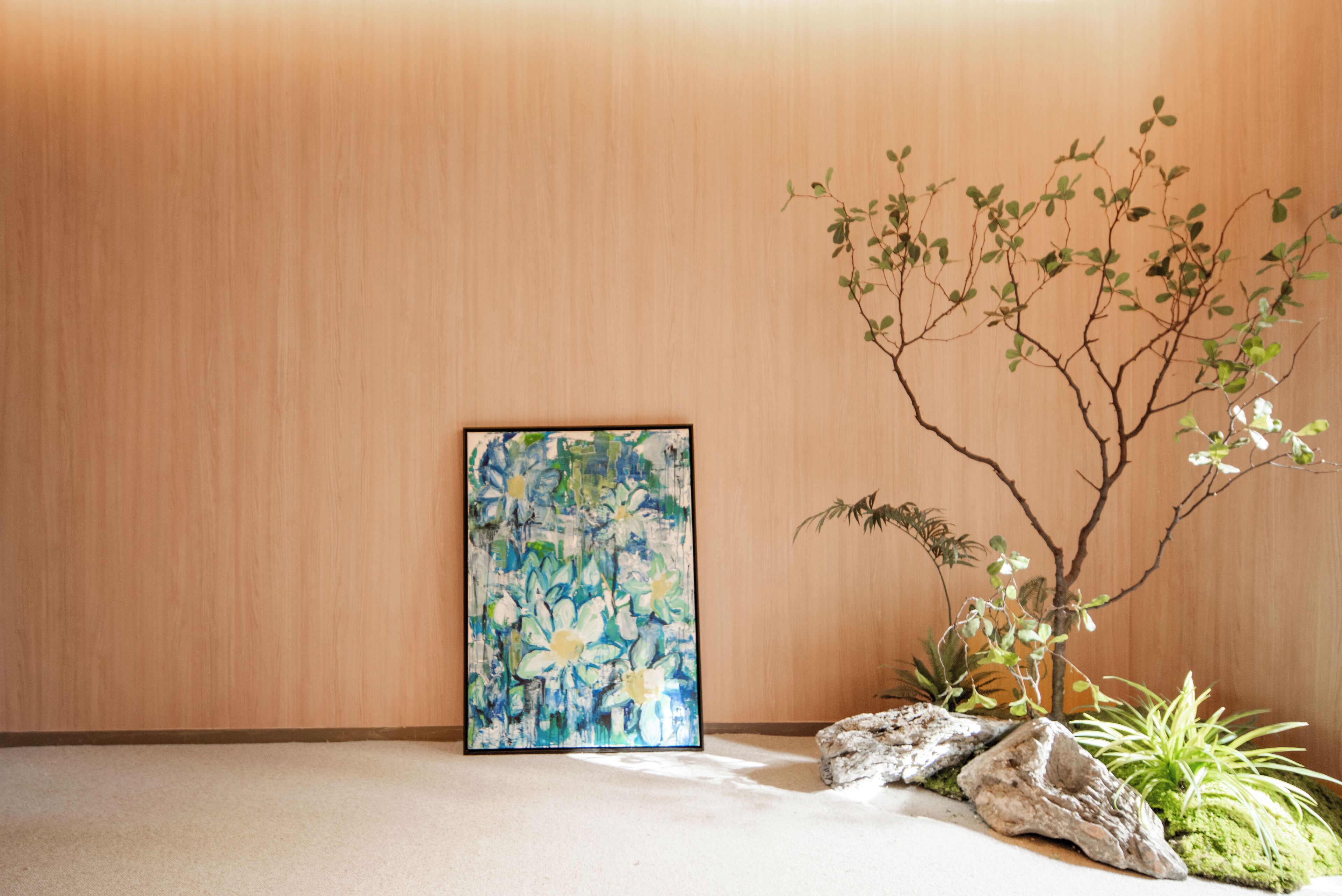 A room with a wooden wall, a framed abstract painting, and a bonsai tree.