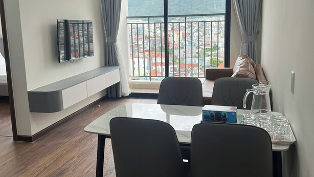 A modern living room with a dining area, large windows with curtains, a mounted air conditioner, and a view of a cityscape.