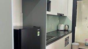 A compact kitchen with a black refrigerator, white cabinets, a microwave, and a small trash bin.