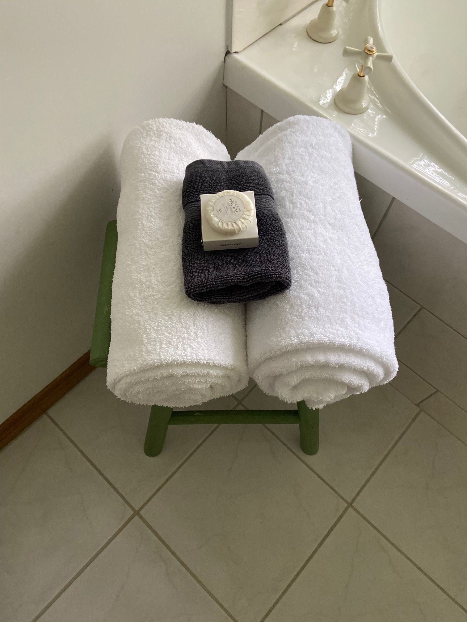 A bathroom with a green stool holding two white towels and a bar of soap.