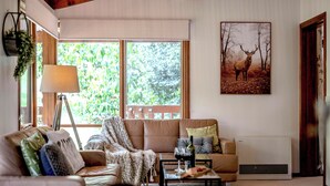 A cozy living room with a sofa, a coffee table with wine glasses, a lamp, and a deer painting on the wall. - Botanica Retreat - Village Spa & Stay (Olinda)