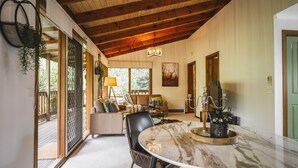A spacious living room with a high ceiling, a marble dining table, and a comfortable seating area. - Botanica Retreat - Village Spa & Stay (Olinda)
