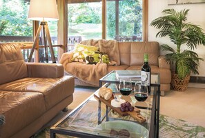 A living room with a leather sofa, a glass coffee table with food and drinks, a lamp, and a view of greenery outside. - Botanica Retreat - Village Spa & Stay (Olinda)
