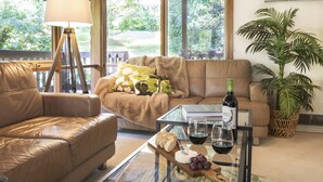 A living room with a leather sofa, a glass coffee table with food and drinks, a lamp, and a view of greenery outside. - Botanica Retreat - Village Spa & Stay (Olinda)