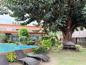 A pool area with lounge chairs, a large tree, and a building with a red roof. - Seaview Beach Resort Dumaguete Beachfront (Sibulan)