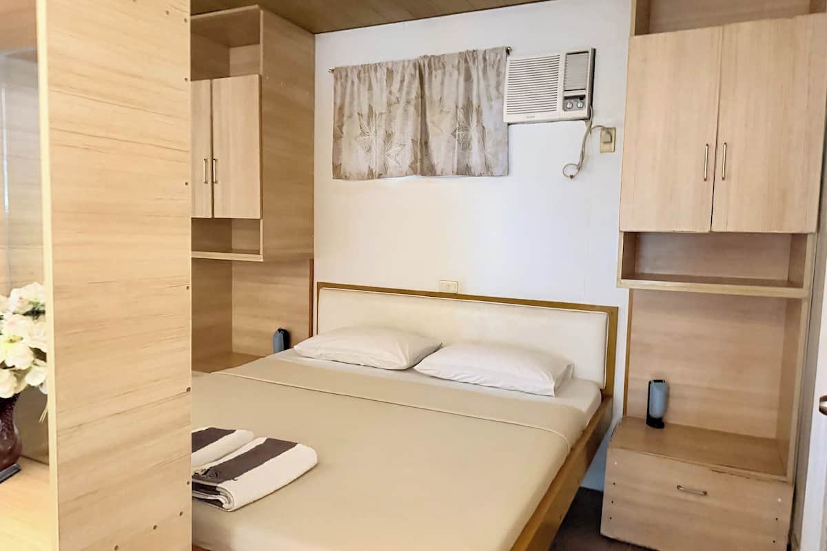 A bedroom with a bed, a nightstand, a wardrobe, a wall-mounted air conditioner, and a curtain.