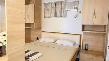 Un dormitorio con cama, mesita de noche, armario, aire acondicionado instalado en la pared y cortina.