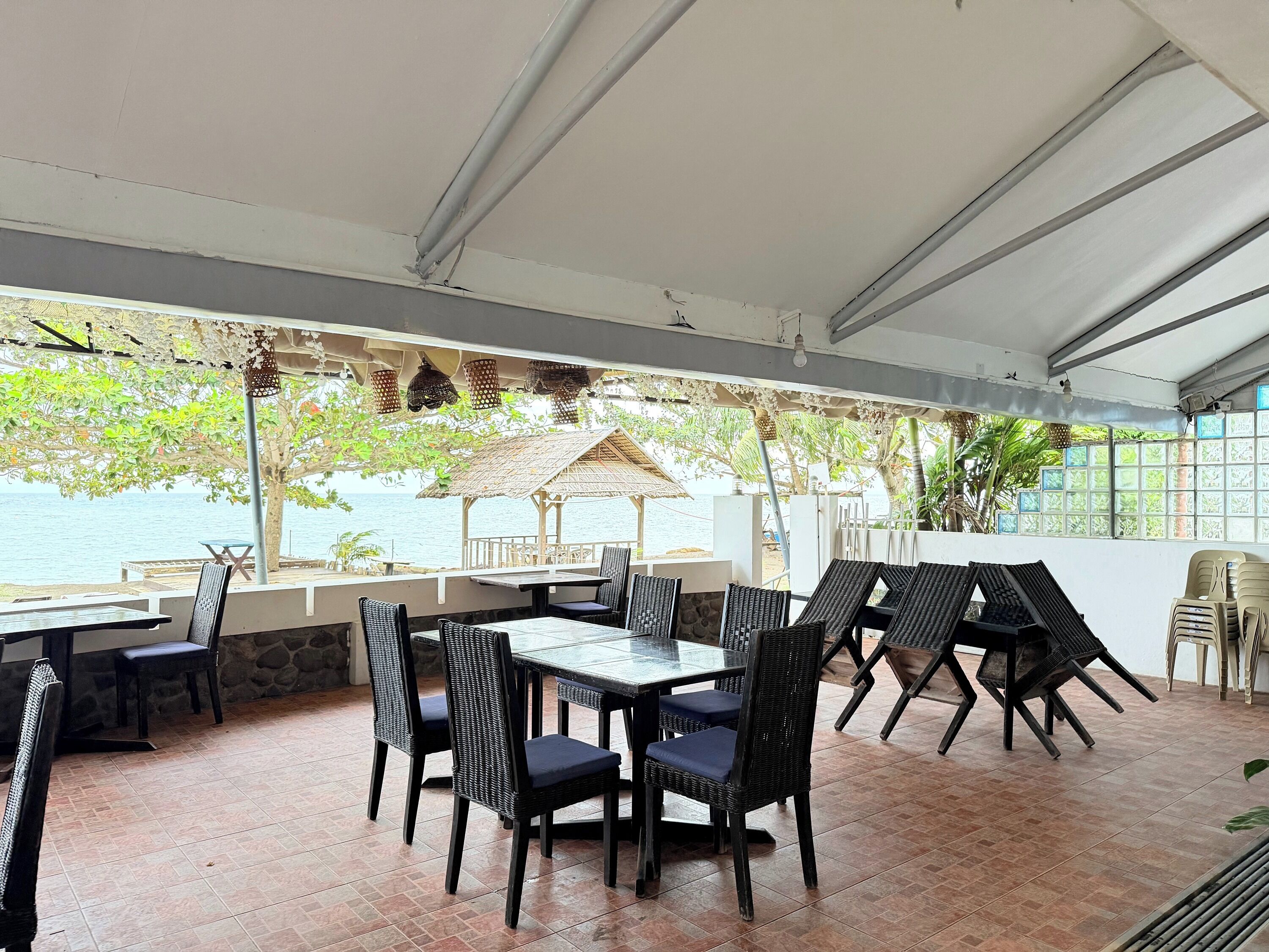 An outdoor dining area with tables and chairs, overlooking a beach and the sea.