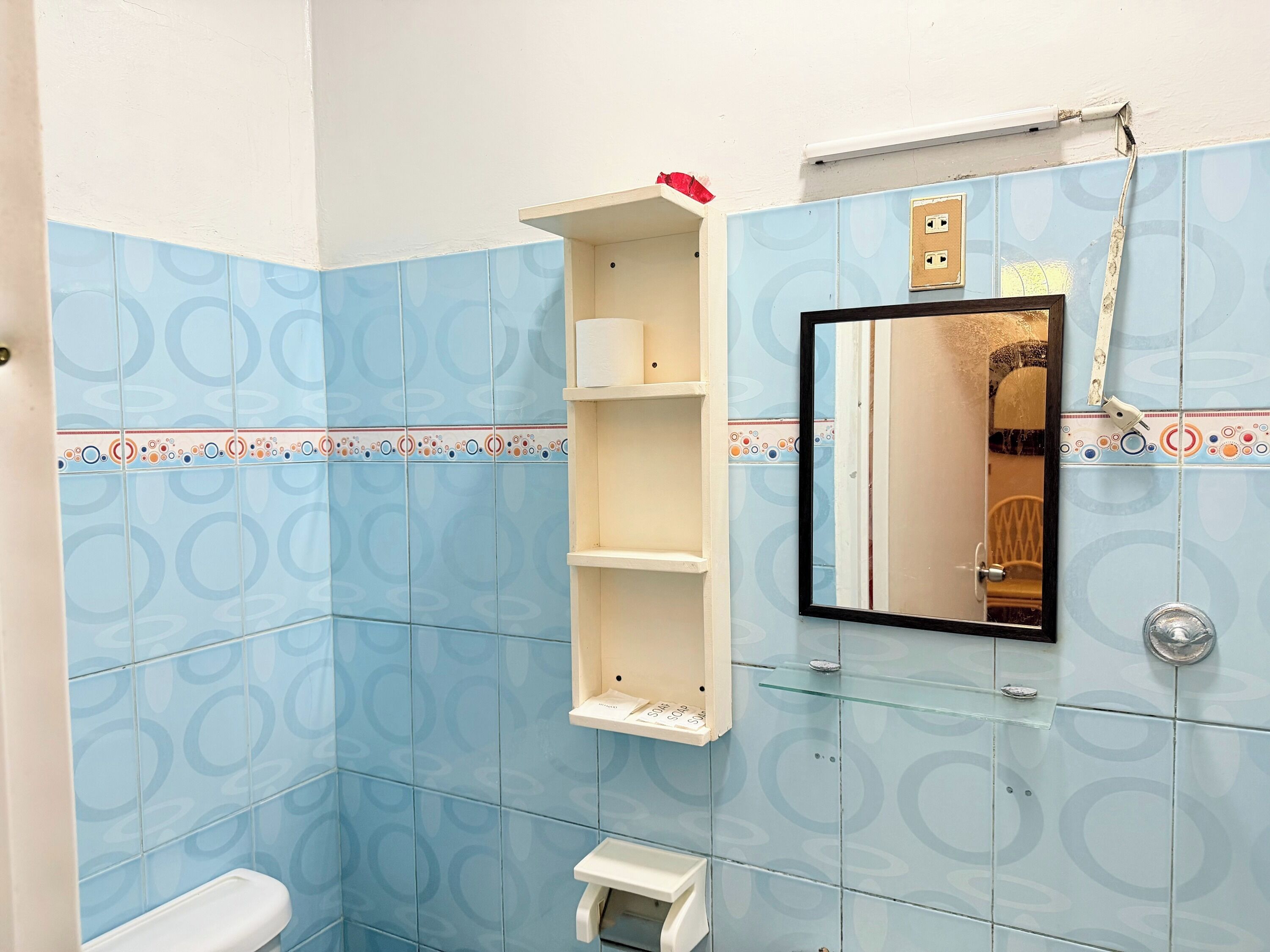 Un baño con azulejos azules estampados, inodoro blanco, repisa de cristal y espejo con marco negro.