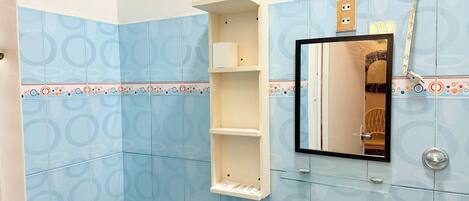 Un baño con azulejos azules estampados, inodoro blanco, repisa de cristal y espejo con marco negro.