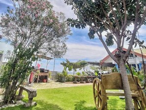 A garden with a wooden cart, a stone bench, and a house with a red roof. - Seaview Beach Resort Dumaguete Beachfront (Sibulan)