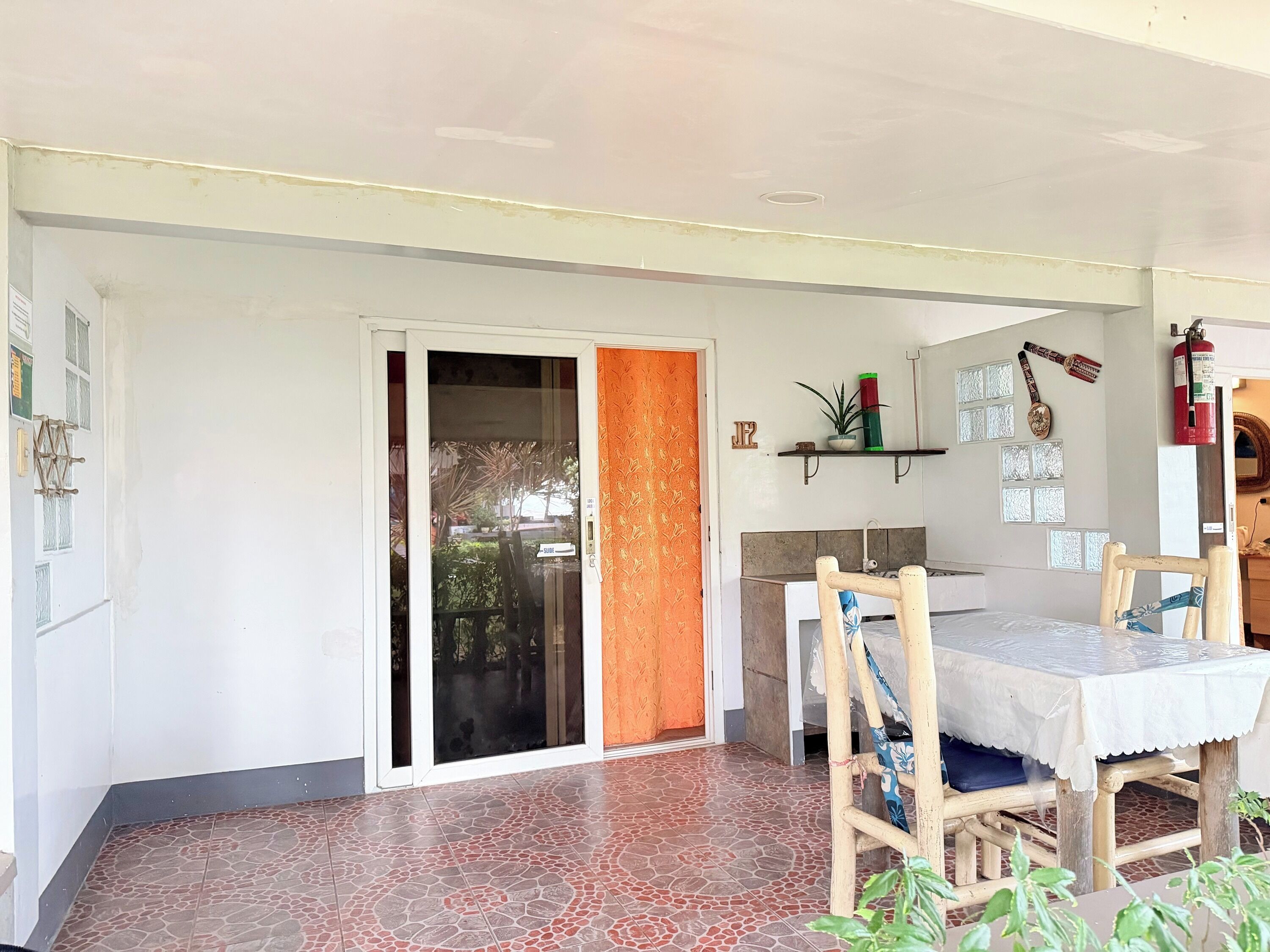 A room with a tiled floor, a sliding glass door, a table with chairs, a shelf with decorative items, and a fire extinguisher.