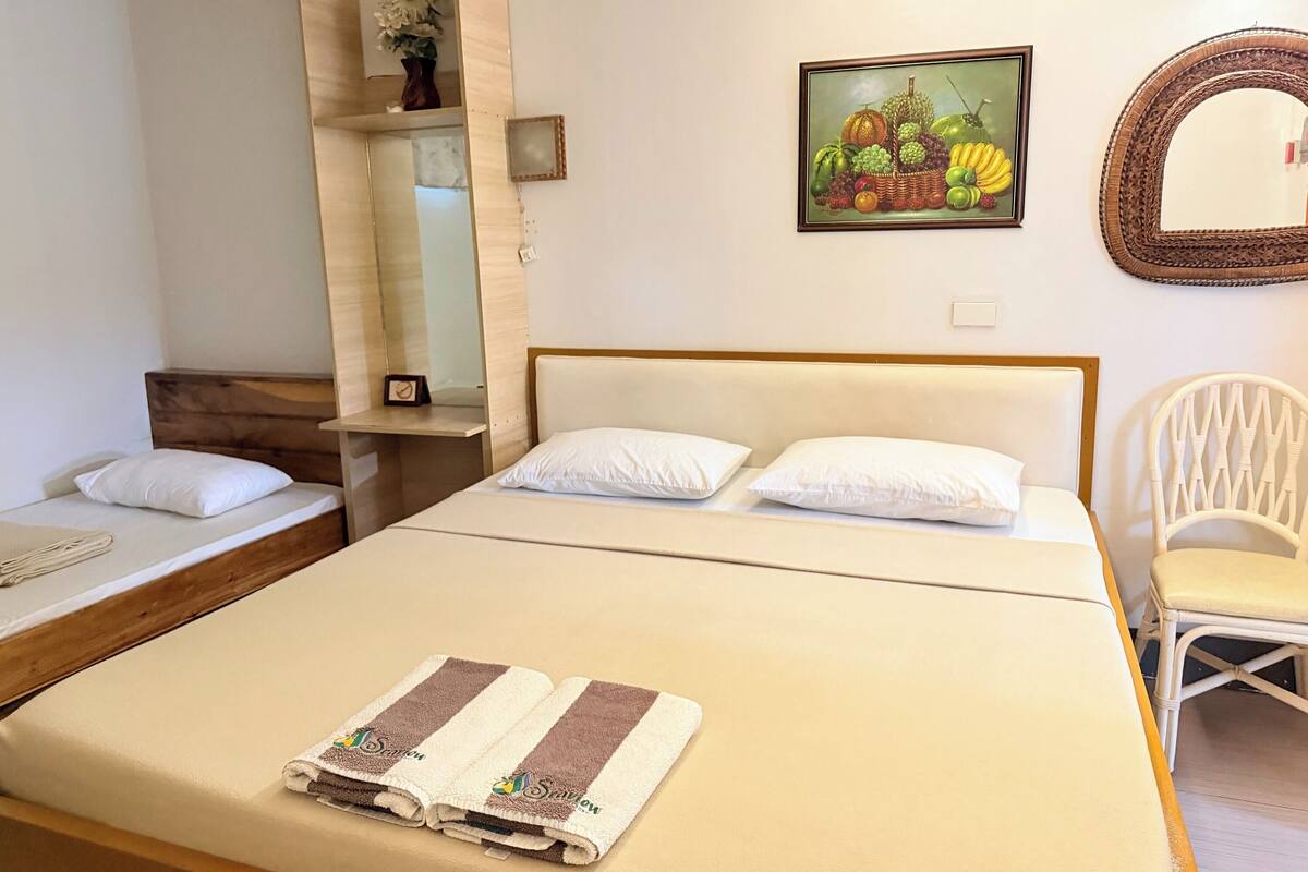 A hotel room with a bed, a chair, a small table, a mirror, and a painting on the wall.