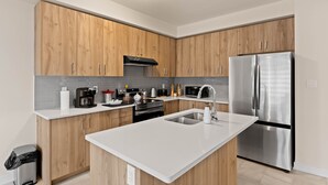 Een moderne keuken met houten kastjes, een roestvrijstalen koelkast, een wit aanrechtblad en een inbouwoven.