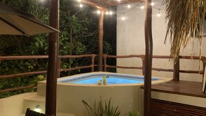 Un bain à remous installé sous une pergola en bois, illuminé de guirlandes lumineuses, et entouré d’une végétation luxuriante.