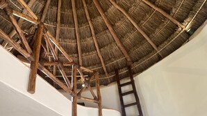 Une pièce avec un plafond haut, des poutres apparentes, un toit de chaume et une échelle en bois.