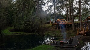 Een rustieke blokhut met een houten terras en een klein zitgedeelte aan een vijver.