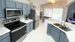 A modern kitchen with grey cabinets, stainless steel appliances, a built-in oven, and a large window with curtains. - Spacious Villa with Private Heated Pool & Office (Kissimmee)