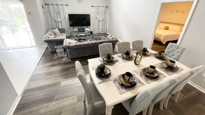 A modern living room with a sofa, TV, and gaming console. A dining area with a table set for four is visible. - Spacious Villa with Private Heated Pool & Office (Kissimmee)