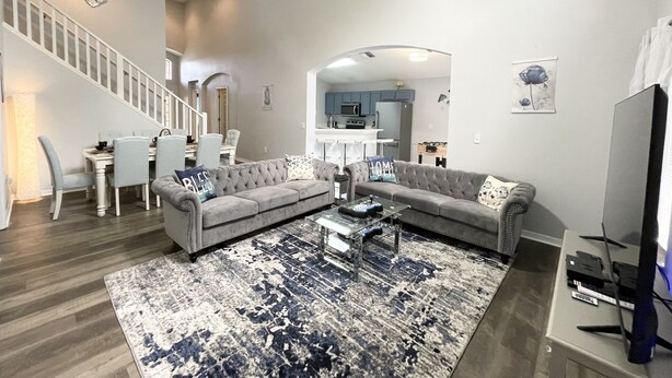 A modern living room with a grey sectional sofa, a coffee table, and a patterned rug. A staircase with white railings leads to an upper level. - Spacious Villa with Private Heated Pool & Office (Kissimmee)