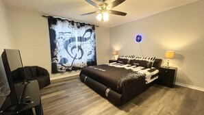 A bedroom with a bed, a ceiling fan, a piano, and a wall with a decorative light. - Spacious Villa with Private Heated Pool & Office (Kissimmee)