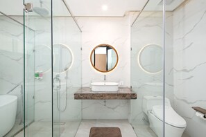 Un baño moderno con ducha de vidrio, tocador de mármol, espejo redondo y un inodoro.