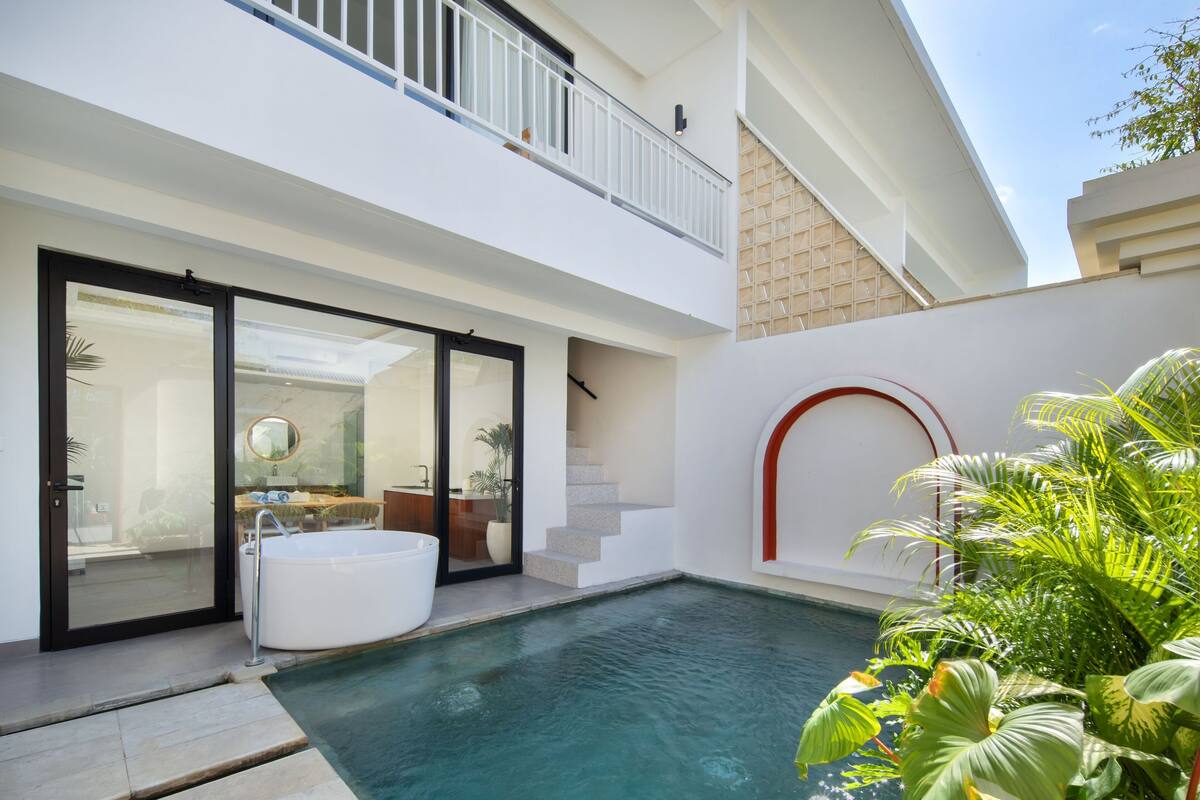 A modern house with a swimming pool, a hot tub, and a staircase leading to a balcony.