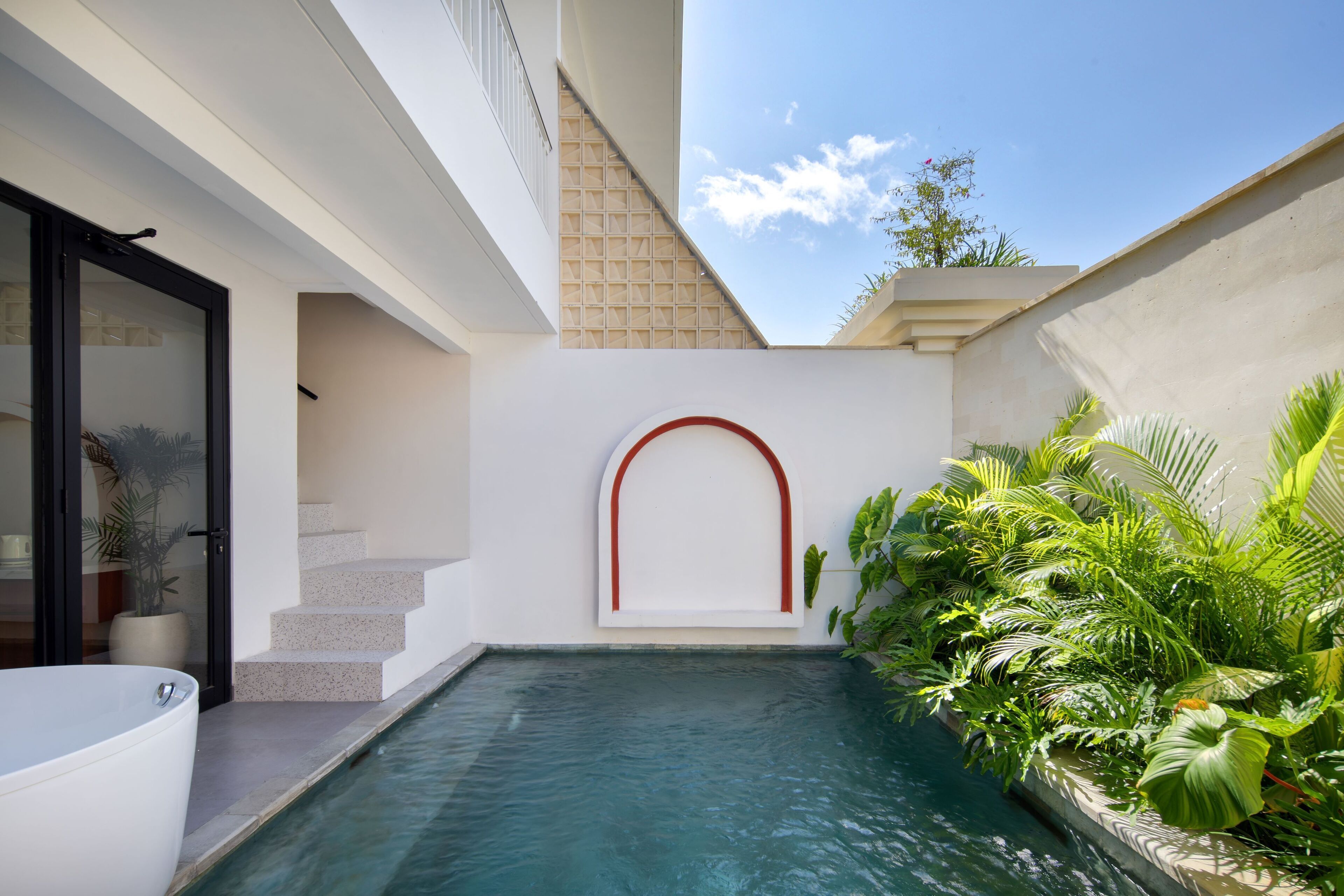 Un espace piscine extérieur moderne, avec une piscine à l’eau d’un bleu limpide, un escalier menant à un niveau supérieur et une végétation luxuriante qui entoure la piscine.