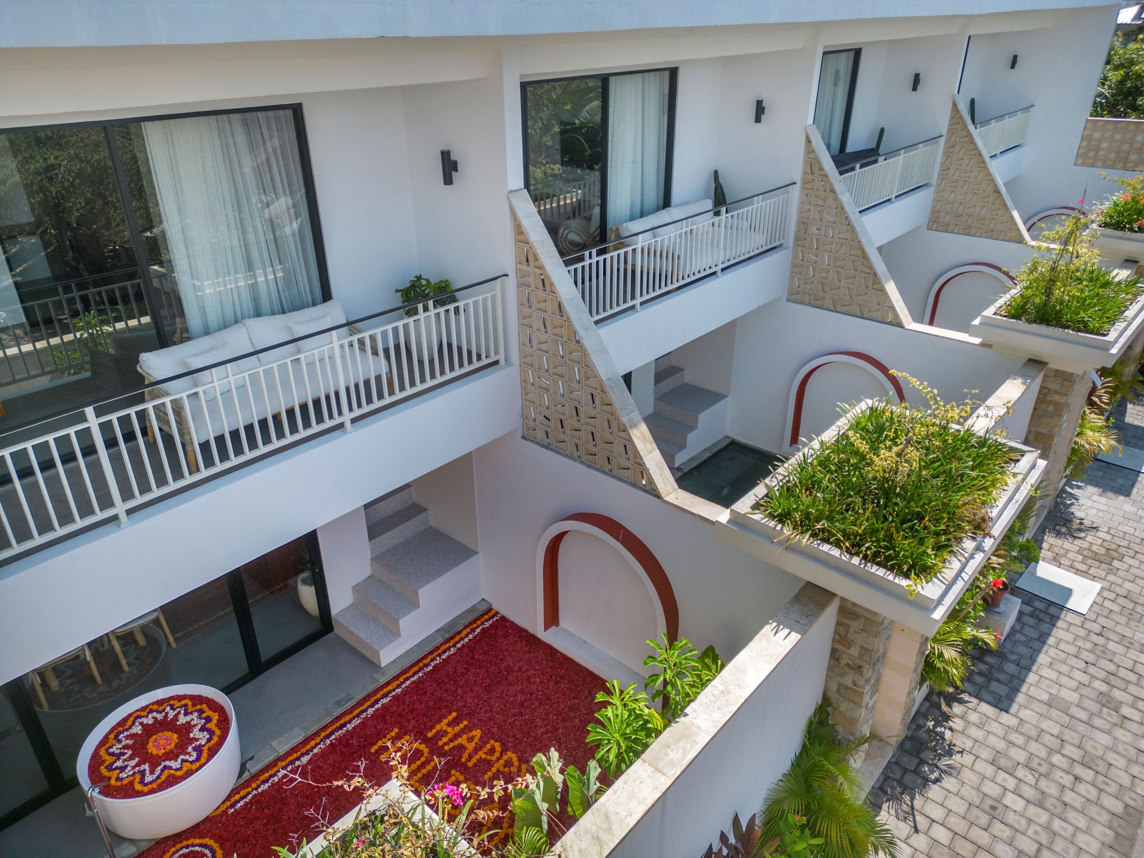 A multi-level hotel with balconies, a red carpet with 'WELCOME' written on it, and potted plants.