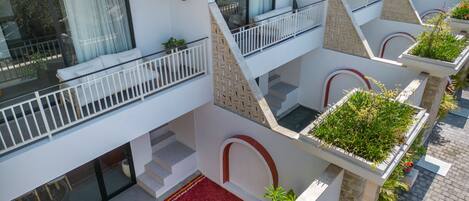 A multi-level hotel with balconies, a red carpet with 'WELCOME' written on it, and potted plants.