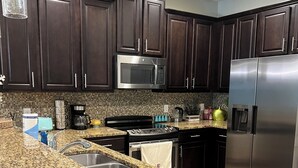 A kitchen with dark wooden cabinets, a stainless steel refrigerator, a granite countertop, and a microwave. - ChampionsGate Townhome + Fast WiFi, Beautiful Kitchen. Oasis Pool & Jacuzzi. (Davenport)