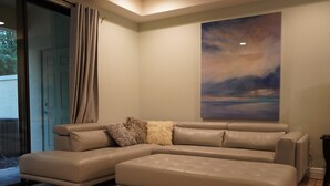 A modern living room with a sectional sofa, a large abstract painting, and a glass door leading outside. - ChampionsGate Townhome + Fast WiFi, Beautiful Kitchen. Oasis Pool & Jacuzzi. (Davenport)