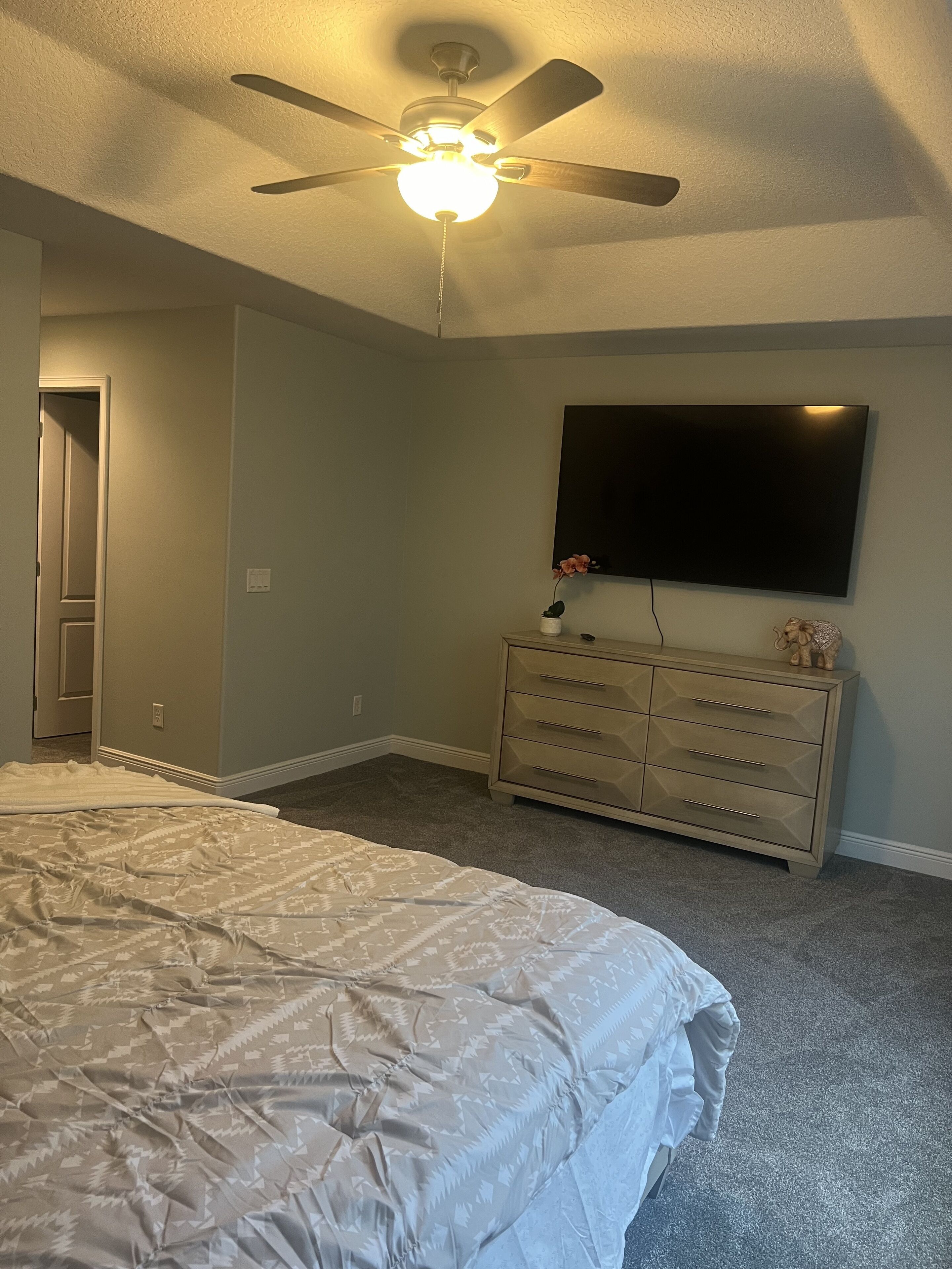 Une chambre à coucher avec un lit, une commode, un téléviseur et un ventilateur de plafond.