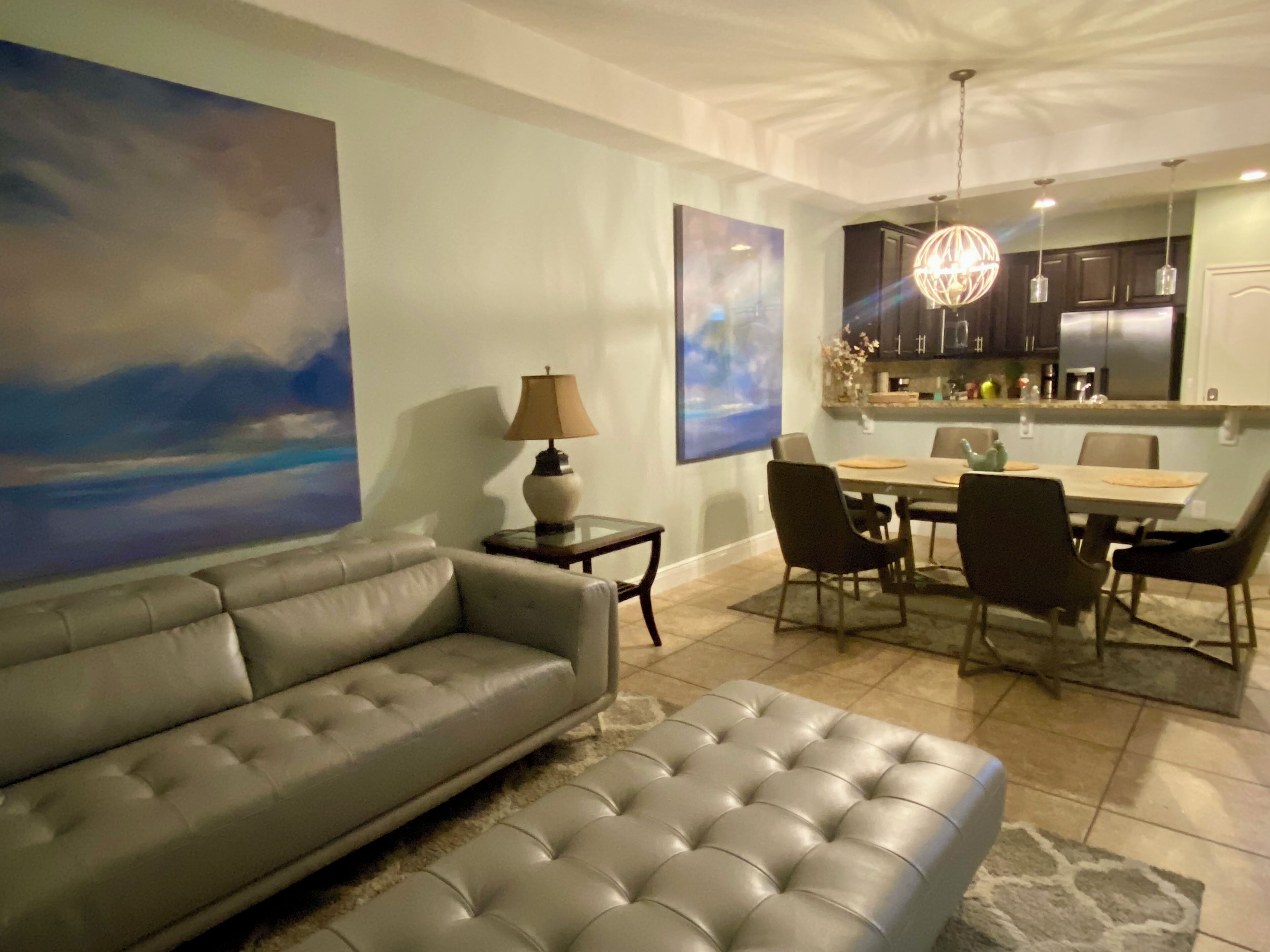 A modern living room with a grey sofa, a dining area with a table and chairs, and a kitchen in the background.