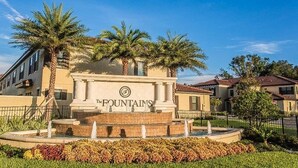 A building with a sign reading "The Fountains" surrounded by palm trees and a fountain. - ChampionsGate Townhome + Fast WiFi, Beautiful Kitchen. Oasis Pool & Jacuzzi. (Davenport)