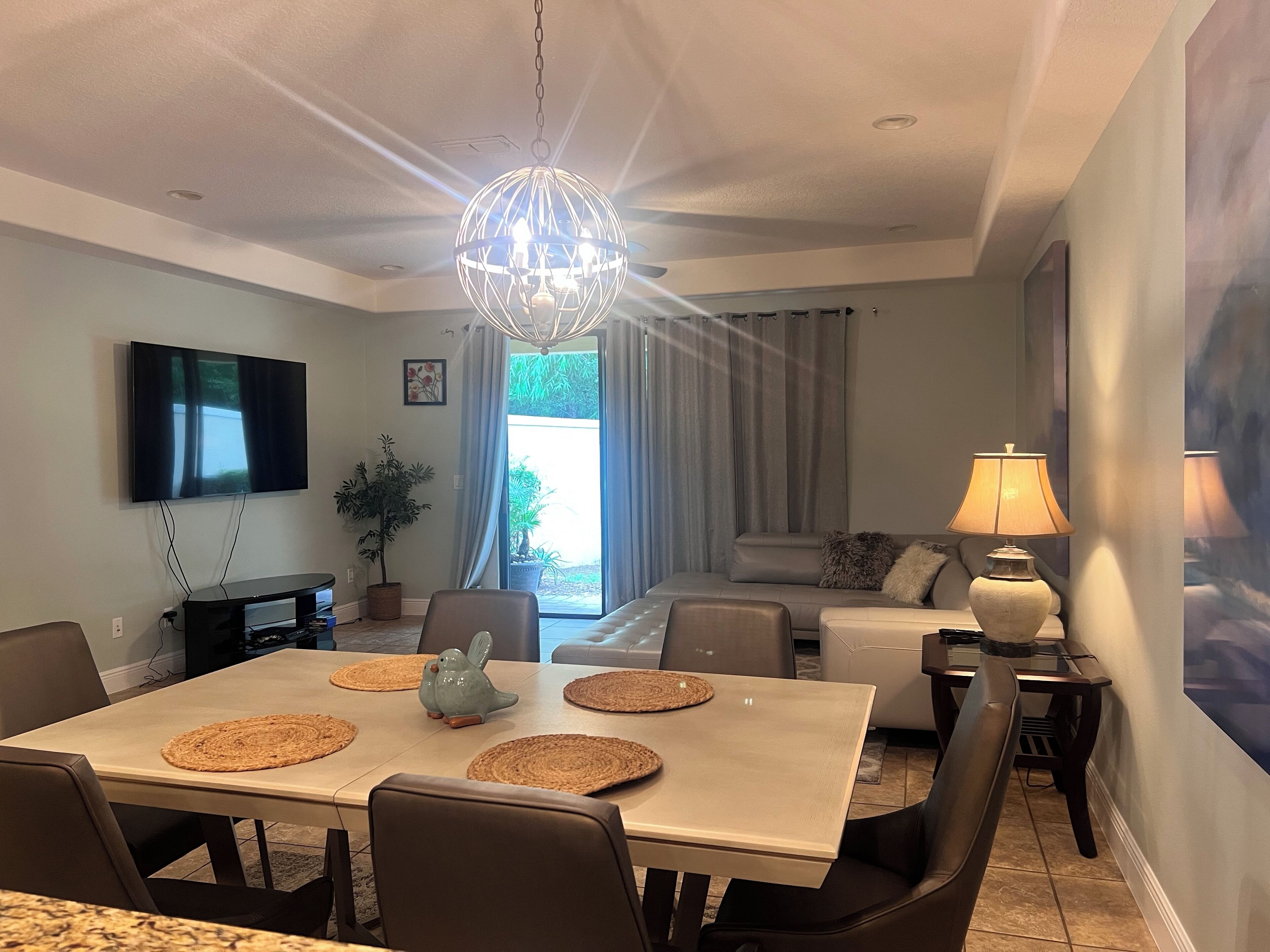 Uma sala de estar moderna com área de jantar, televisão de tela plana, lustre e uma janela grande com cortinas.