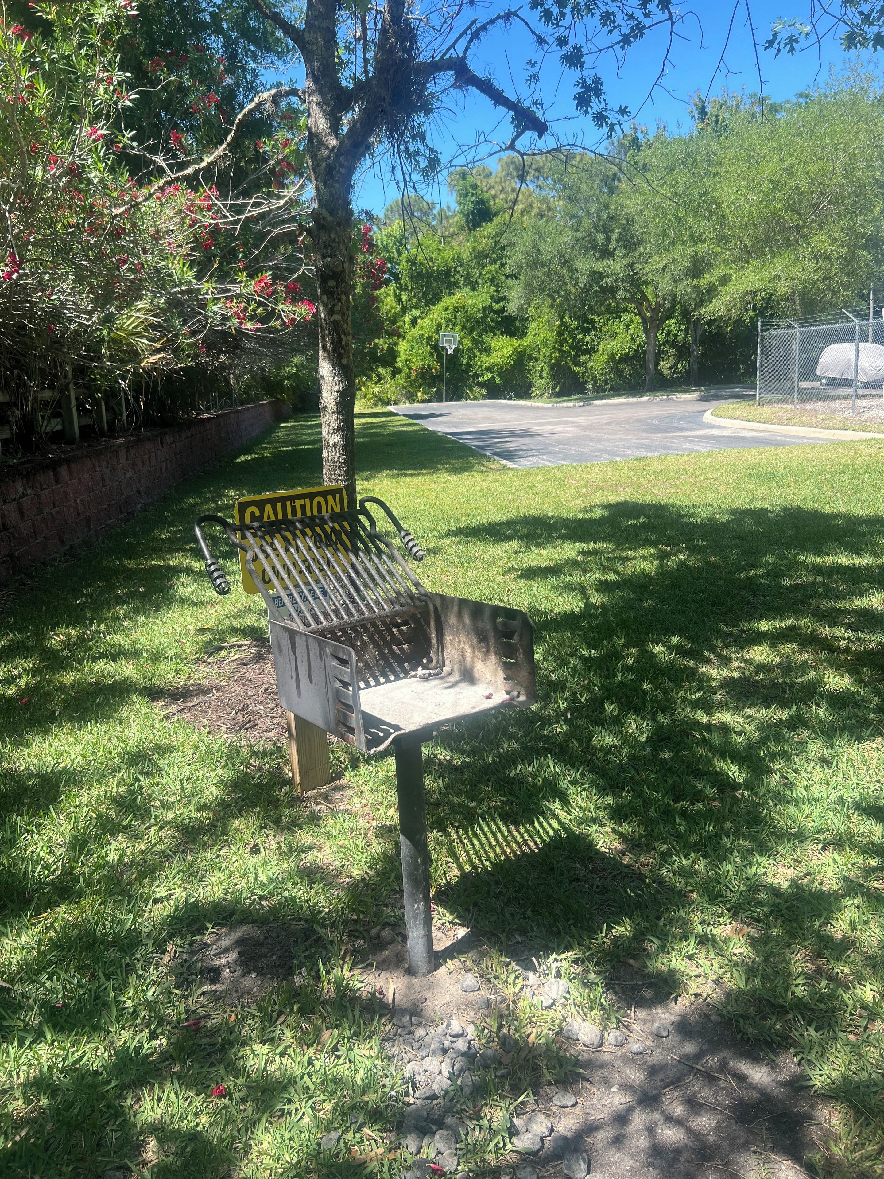 Une grille métallique avec un panneau d’avertissement, un arbre et un terrain de basket-ball en arrière-plan.