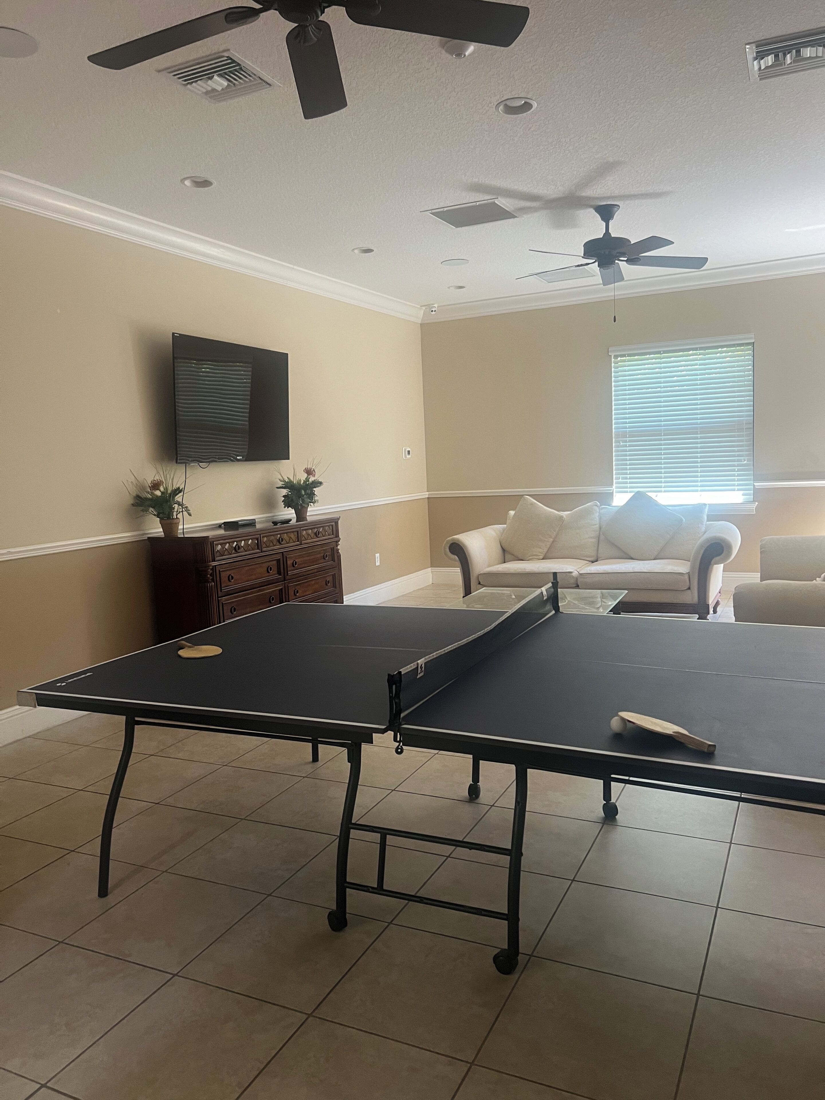Una sala de estar con mesa de ping pong, sofá, televisor y ventiladores de techo.