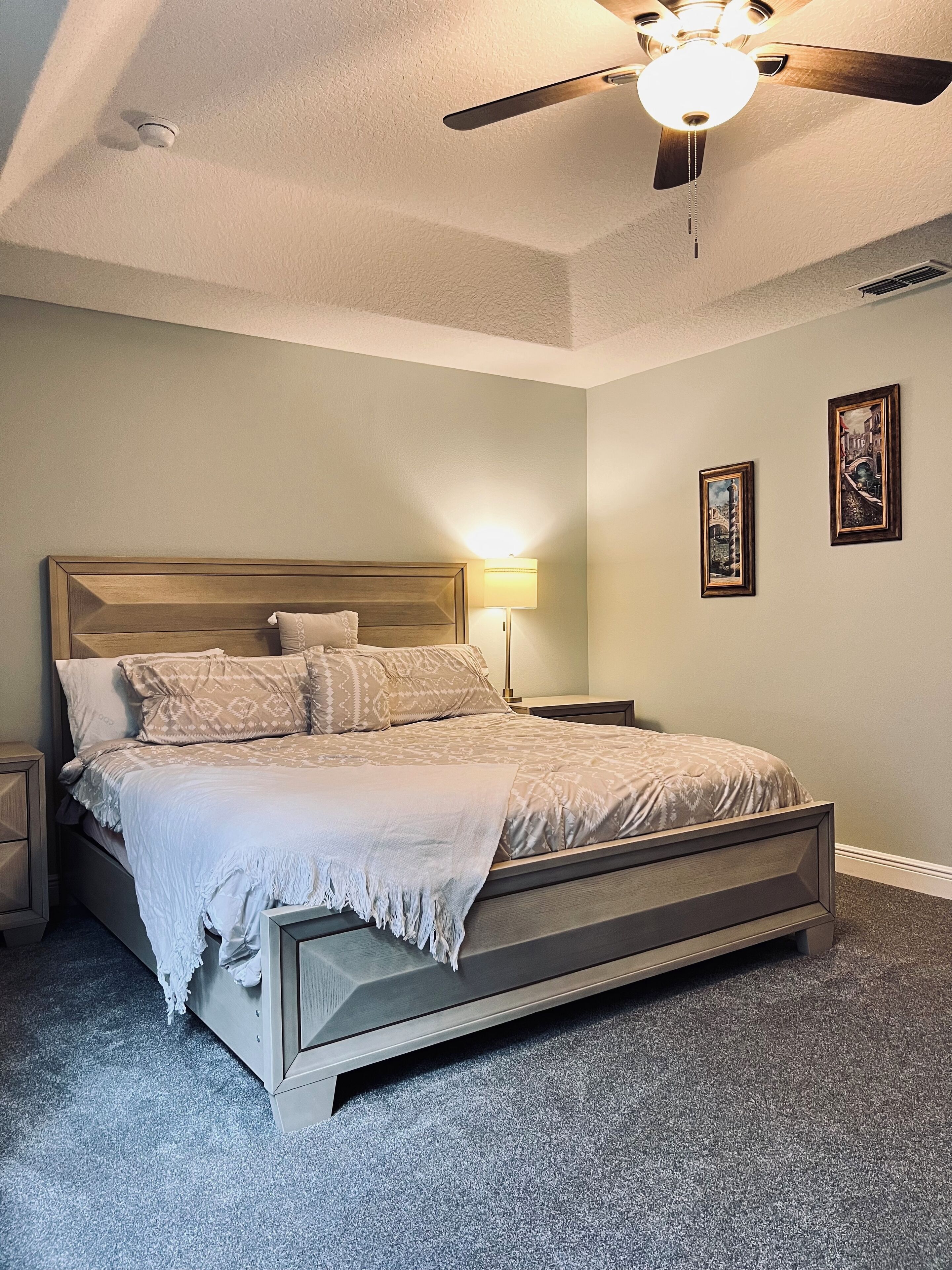 Un dormitorio con cama, mesitas de noche, ventilador de techo y decoración en la pared.