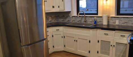 A kitchen with white cabinets, a stainless steel refrigerator, a black countertop, and a window with a view.