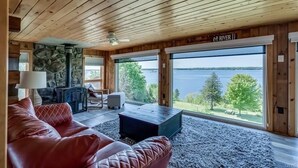 Een gezellig chaletinterieur met een stenen openhaard, een leren bank en grote ramen met uitzicht op een meer.