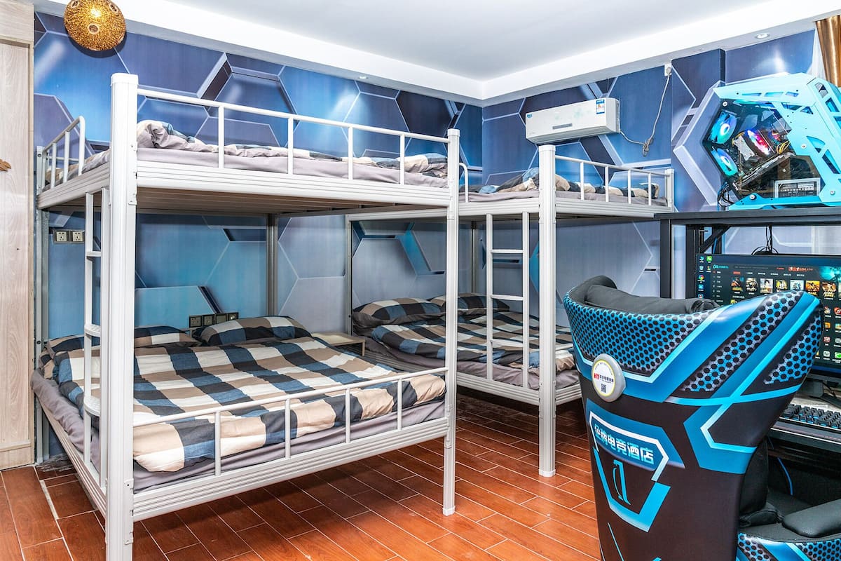 Une chambre avec un lit superposé, une chaise de jeu, un bureau avec un ordinateur et un climatiseur fixé au mur.