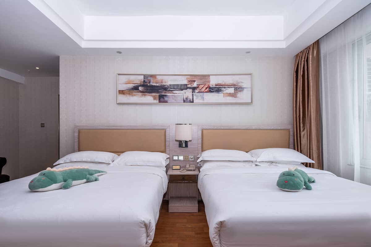 Une chambre d’hôtel avec deux lits, une table de chevet avec une lampe, un téléphone et une œuvre d’art murale.