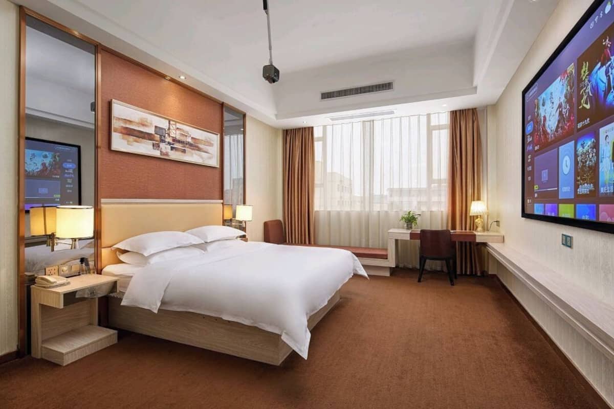Une chambre d’hôtel avec un grand lit, un bureau, une télévision et une fenêtre avec des rideaux.